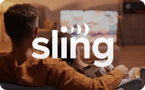 A couple sitting on a couch watching TV in a cozy living room. The Sling logo is overlaid.