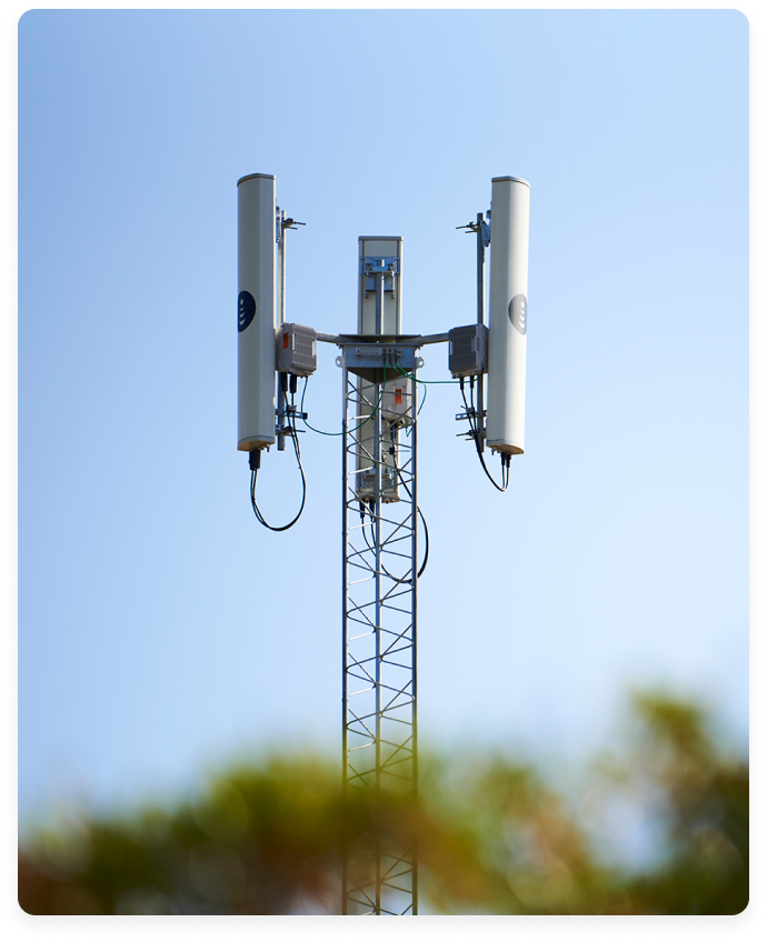 Close-up of a cell tower with antennas and cables against a clear blue sky.